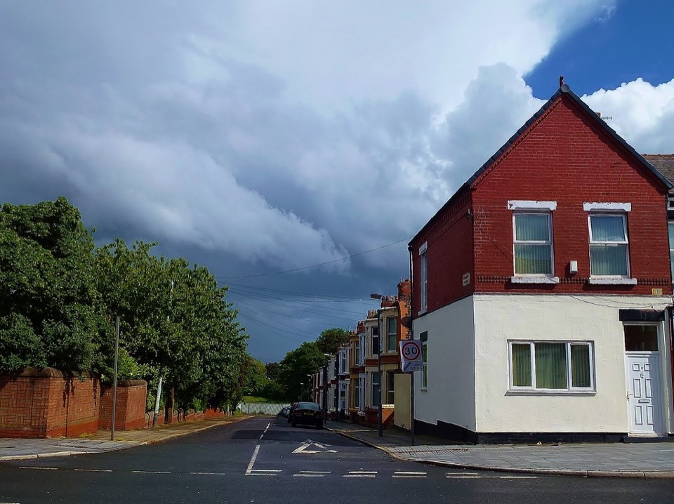 A brick and render corner house at Dingle Lane in Liverpool under a dark sky
