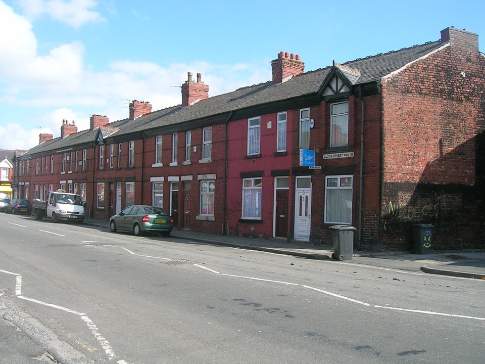 A red brick terrace with a plain gable end on Lloyd Street South in Moss Side, Manchester